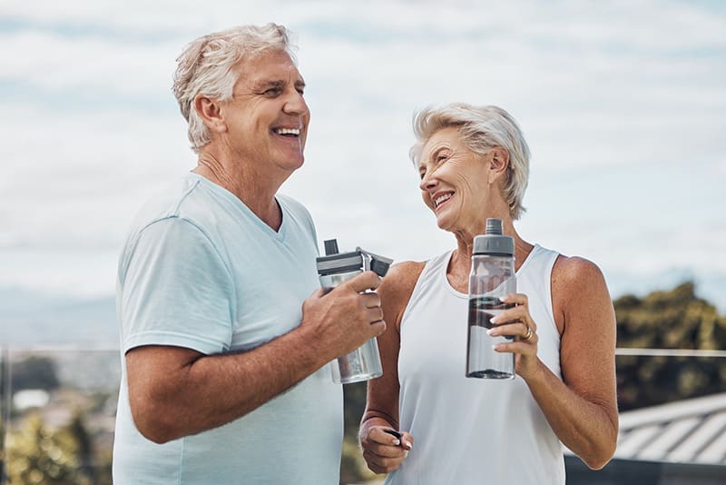 Active senior couple smiling and holding water bottles after outdoor exercise in Jefferson City, TN.