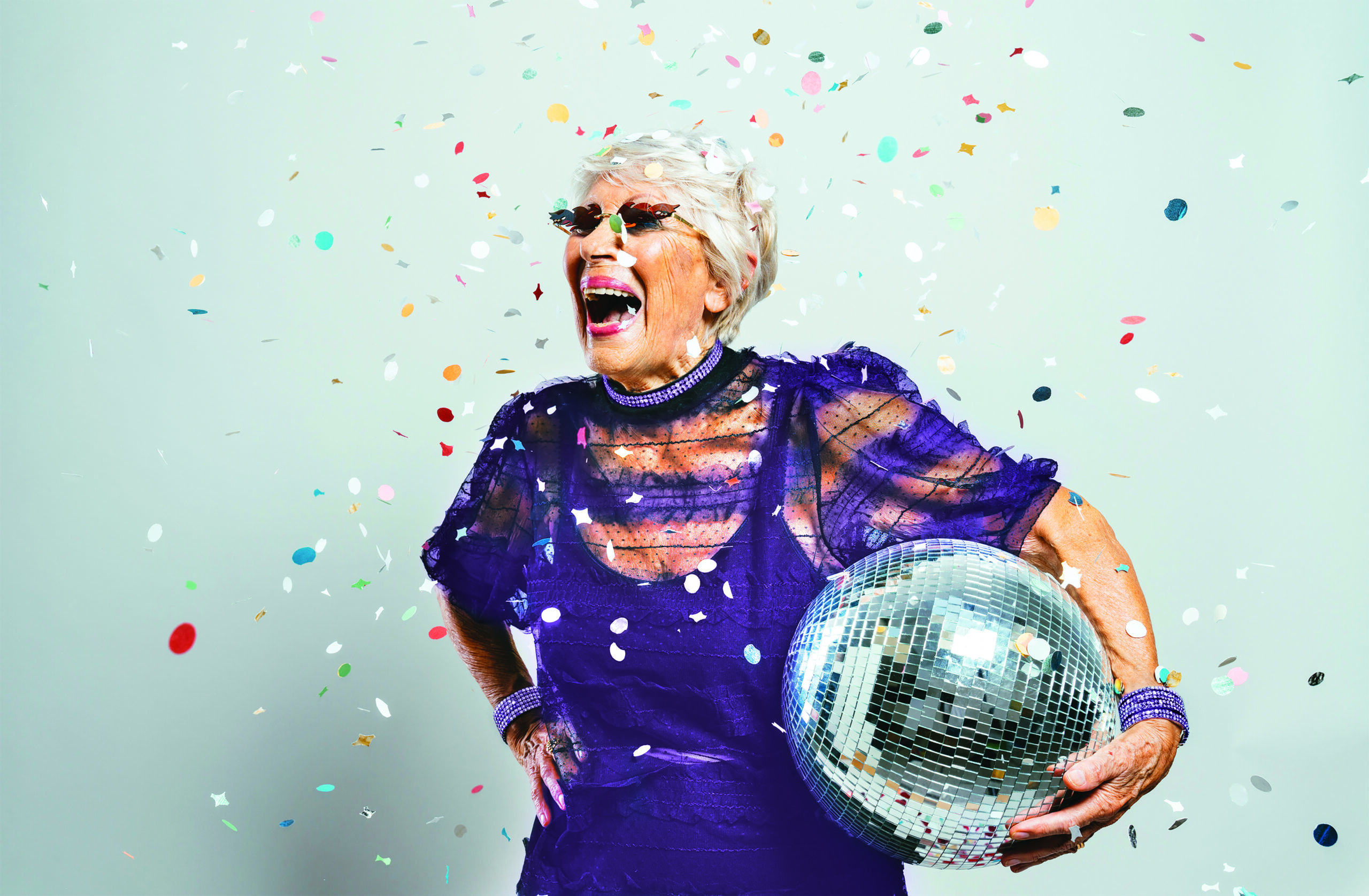 Senior woman in a purple dress laughing and holding a disco ball during a celebration at Charter Senior Living of Jefferson City, TN.